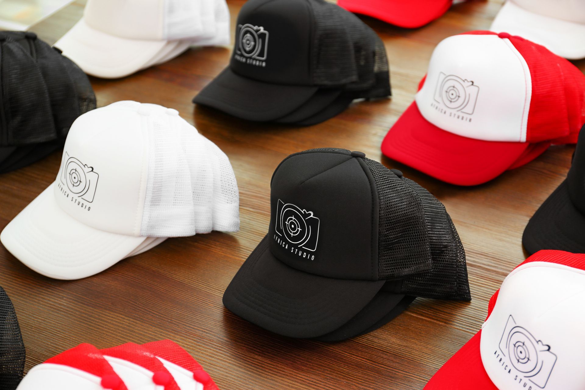 Caps with a logo. Black, white, and red trucker hats displayed on a table.