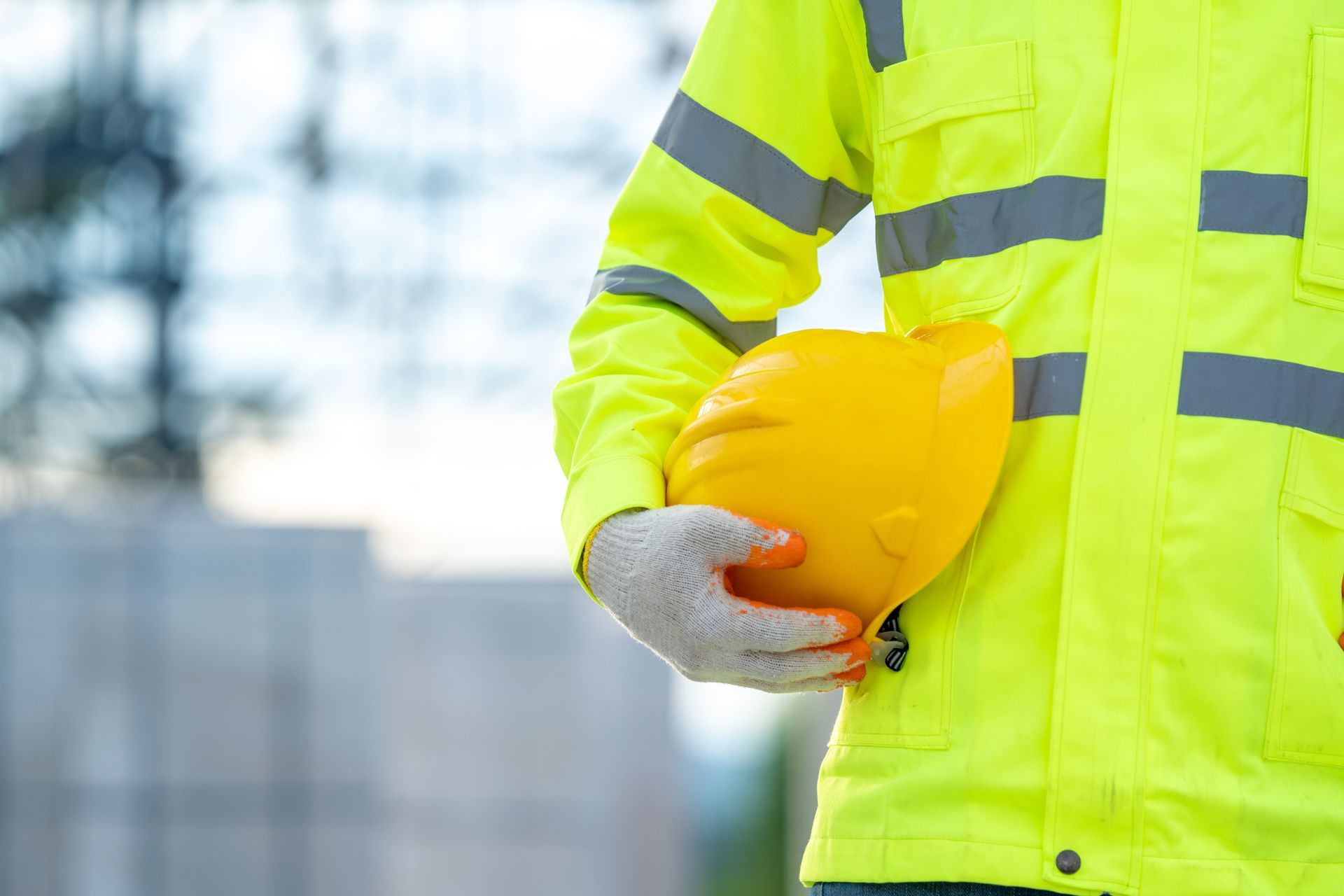 Construction worker holding a yellow hard hat, wearing a high-visibility jacket and gloves.
