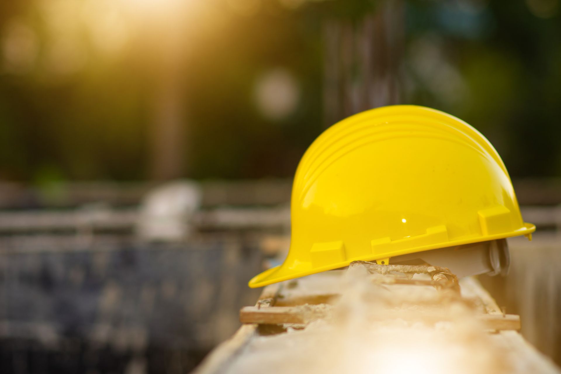Yellow hard hat resting on a pipe, outdoors.