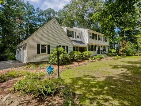 Two-story white house with black shutters, green lawn, trees, and blue pinwheel in front.