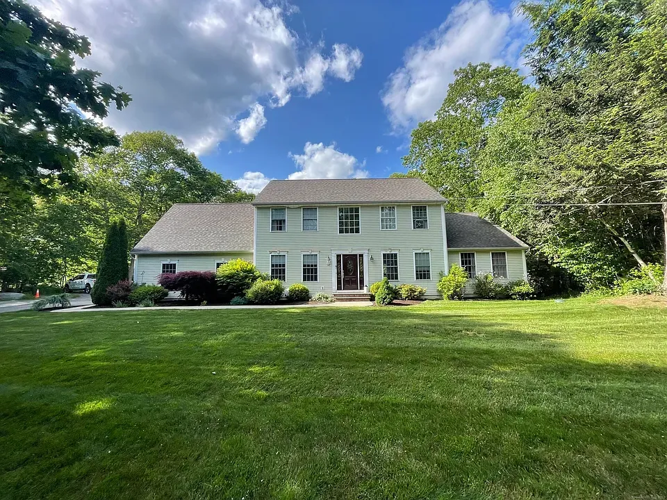 Two-story light green house with green lawn under a partly cloudy sky.