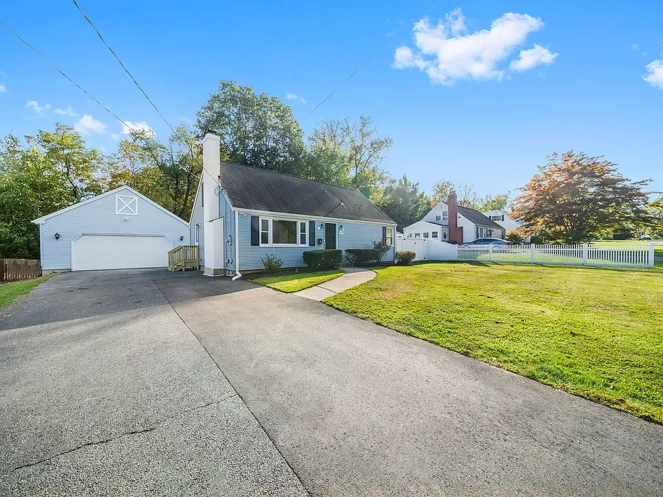 Blue house with detached garage and driveway on a green lawn under a partly cloudy sky.