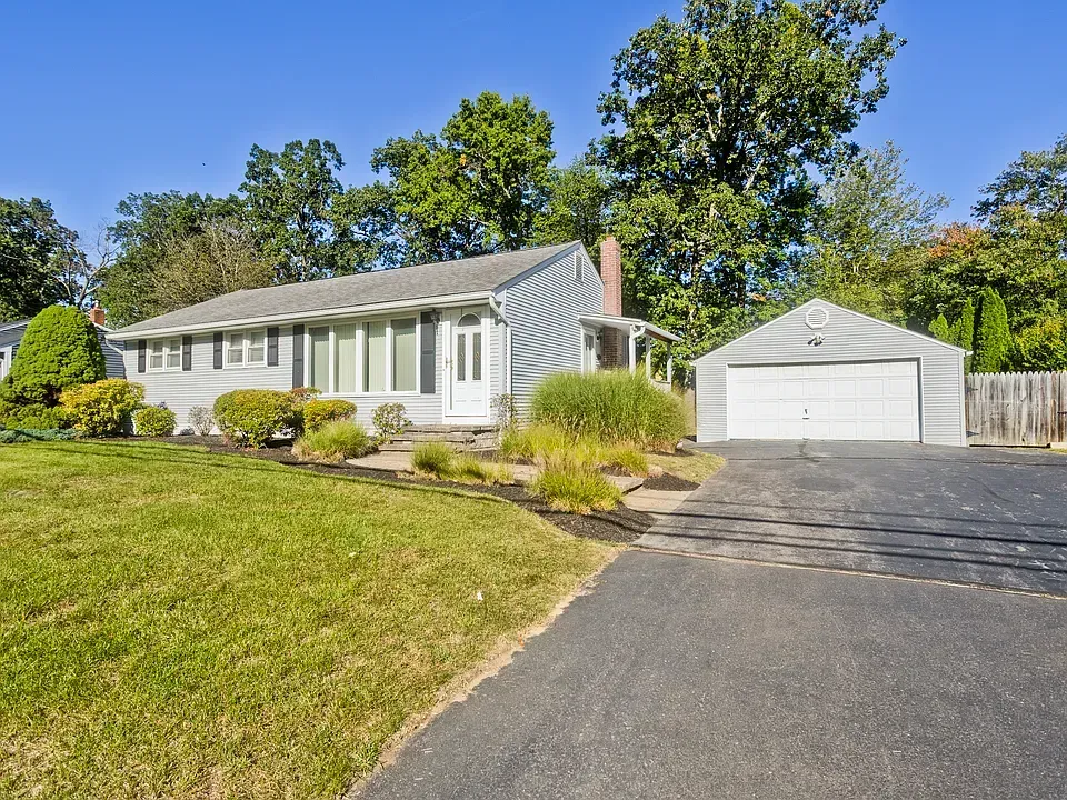 Gray ranch-style house with attached garage, driveway, and lawn on a sunny day.