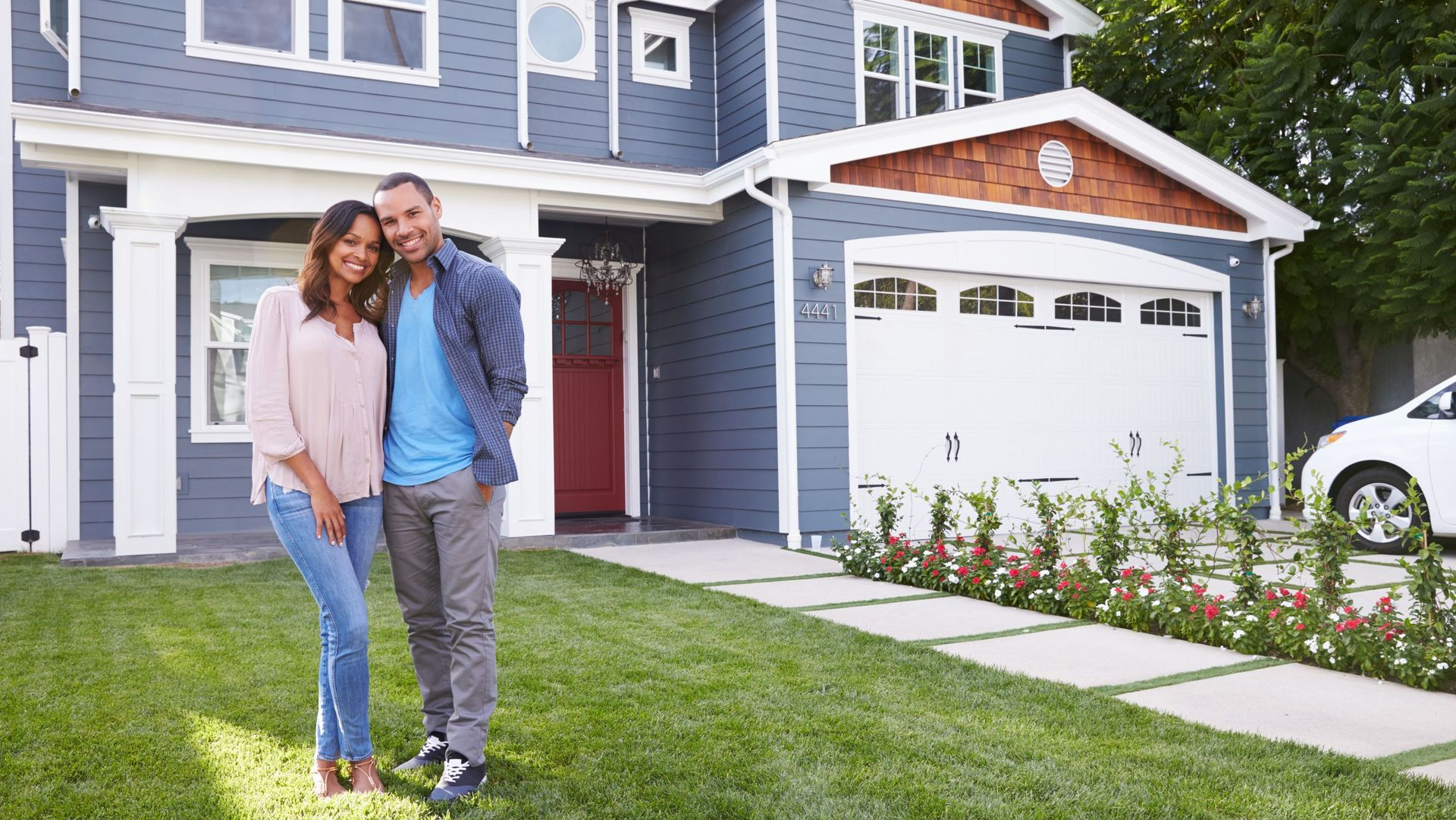 Couple smiling in front of blue house with attached garage and green lawn.