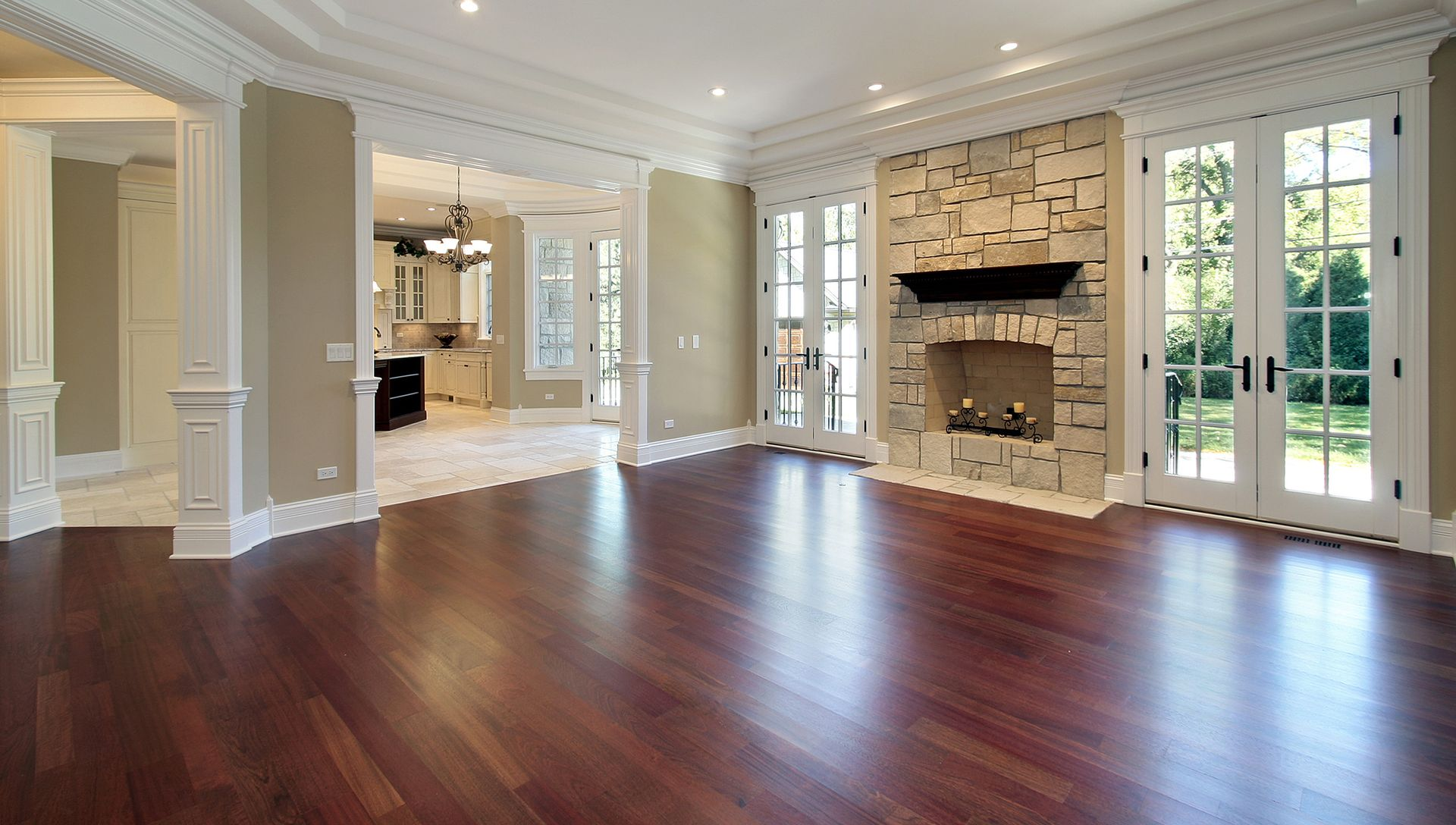 Empty living room with wood floors, stone fireplace, and French doors.