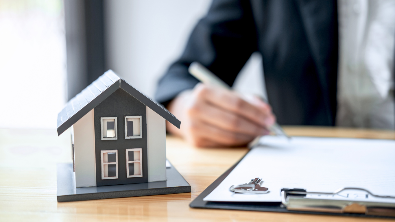 Model house next to a person signing paperwork on a clipboard.