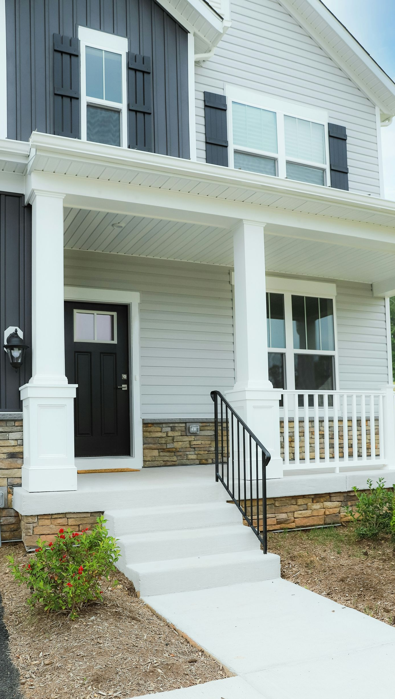 Two-story house with a porch. White siding, black front door, dark gray accent wall, and stone steps.