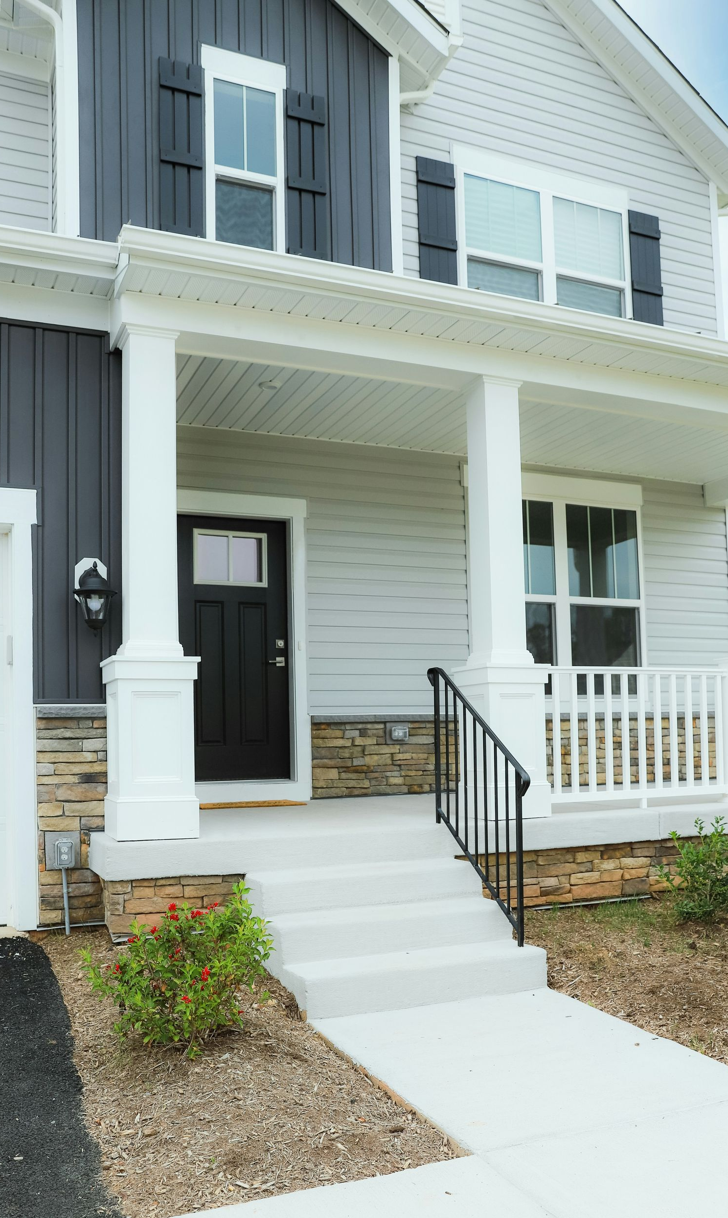 Front view of a two-story house with a porch, white siding, black front door, and gray accents.