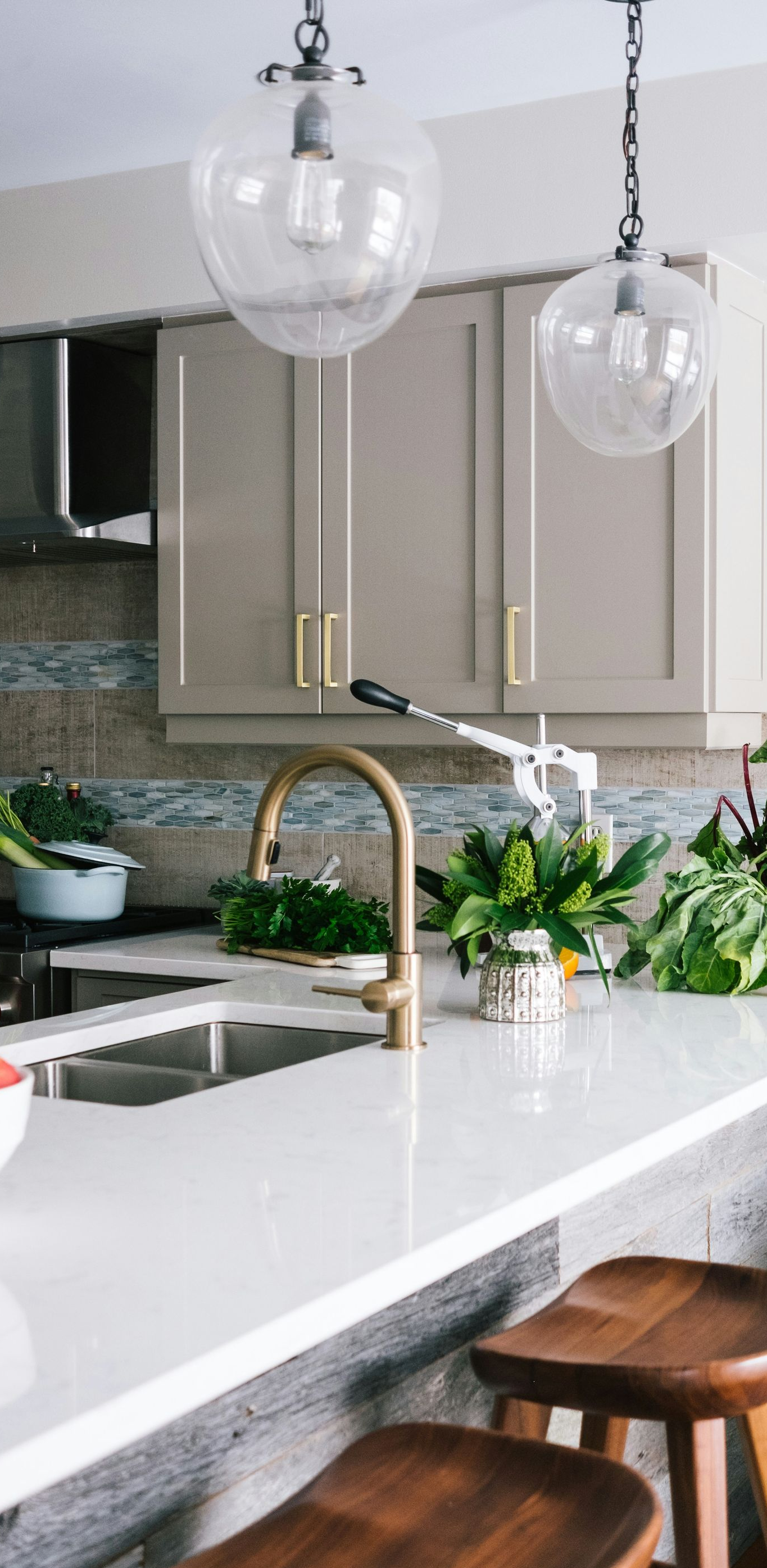 Modern kitchen with white countertop, brown stools, gold faucet, and glass pendant lights.