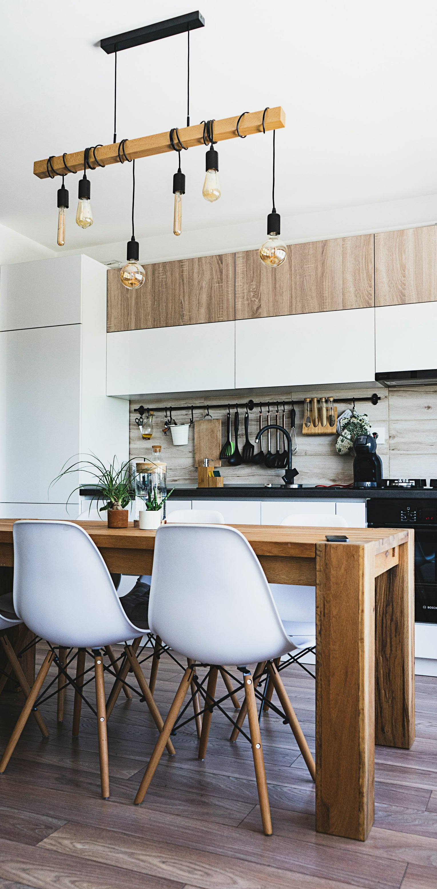 Dining room with wood table and chairs; hanging light fixtures over table near kitchen.