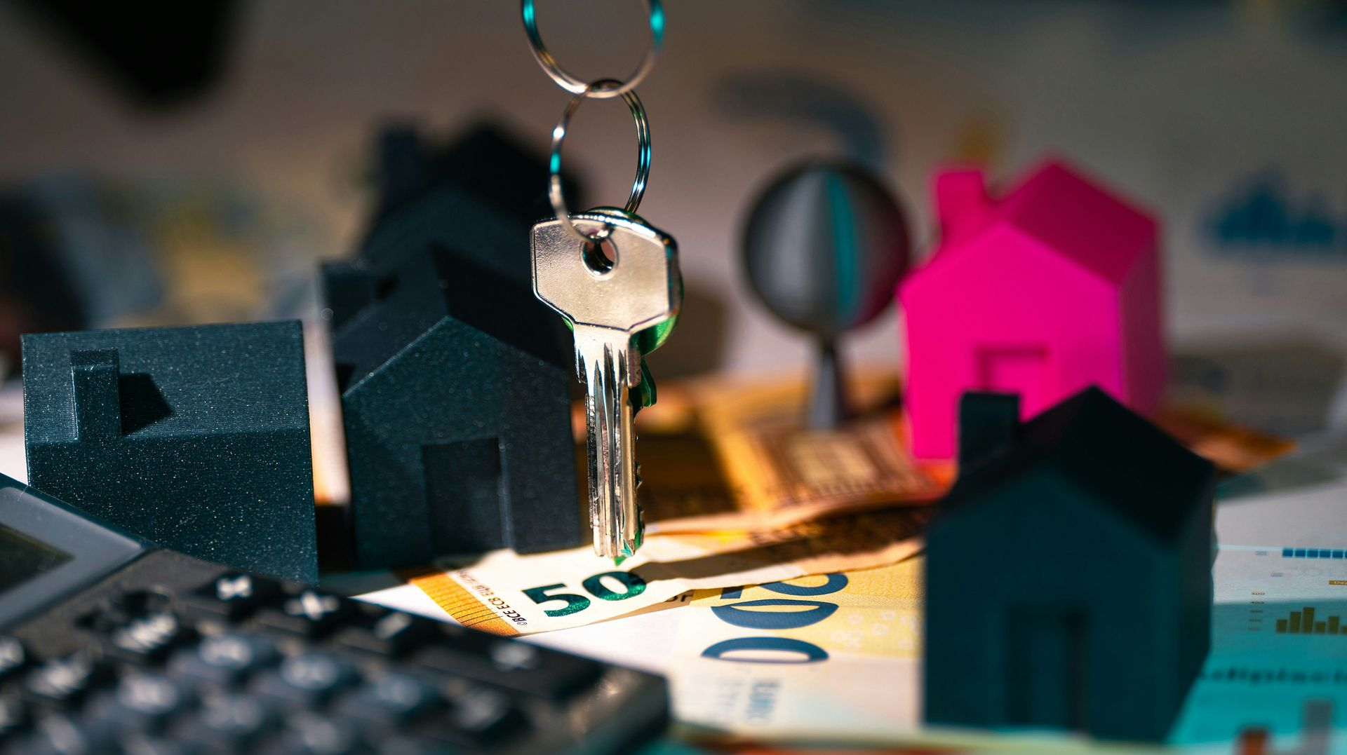 A key on a keychain, tiny house models, calculator, and banknotes on a table.
