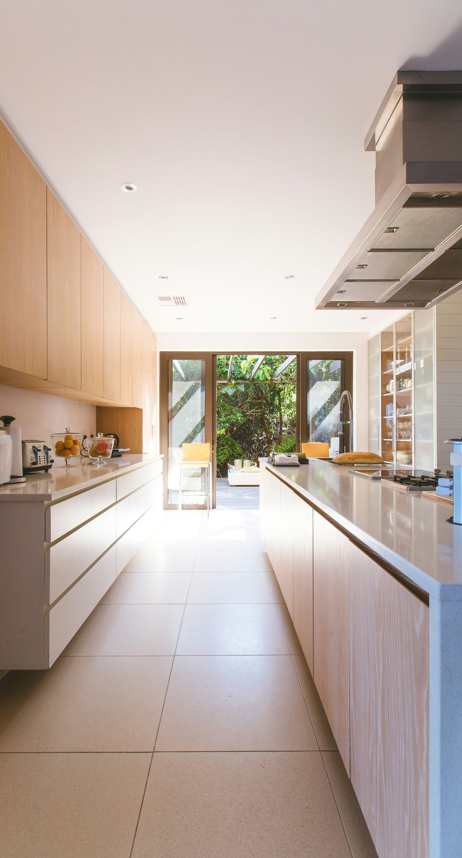 Modern kitchen with long island and cabinets, terrazzo flooring, and a view to a green outdoor space.