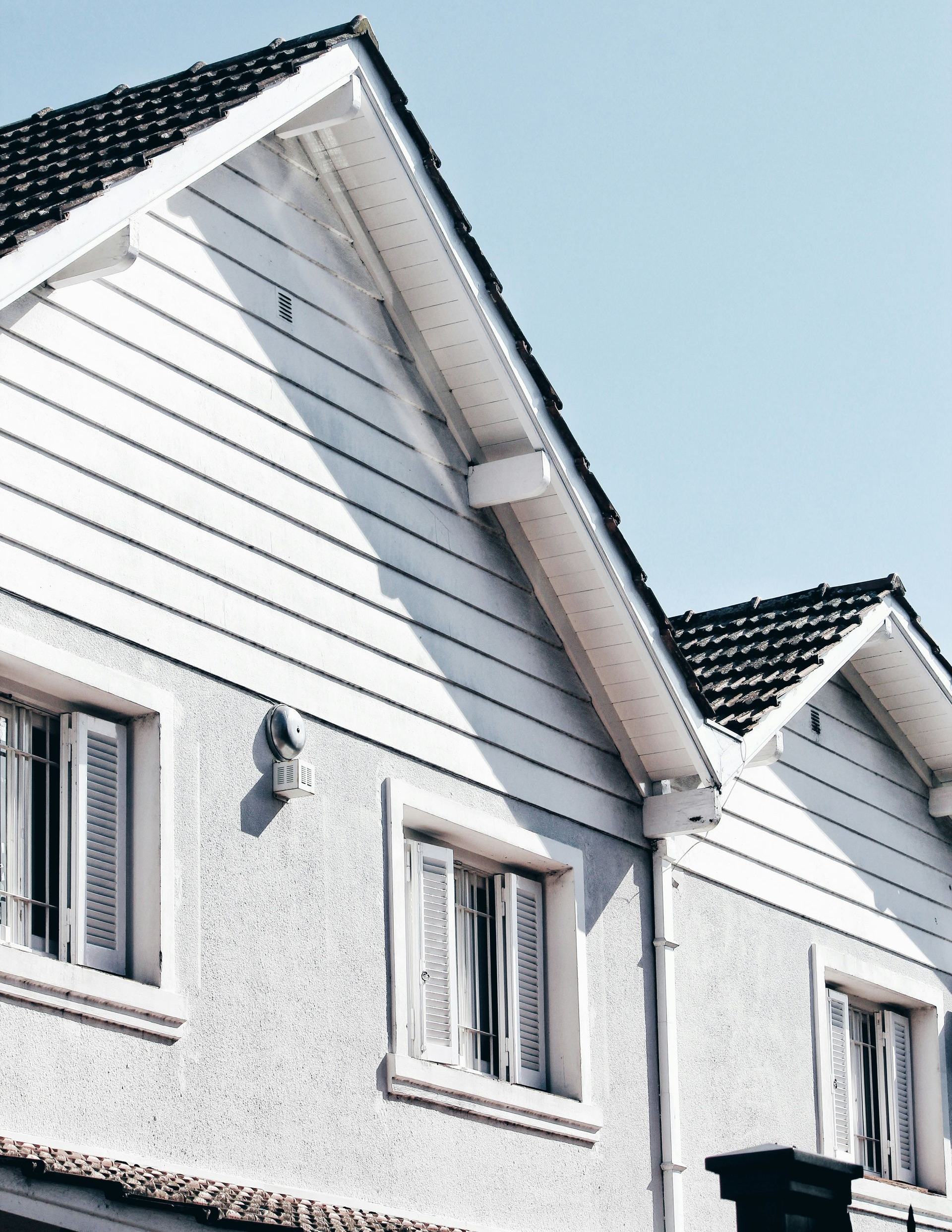 White house with multiple windows and a tiled roof against a blue sky.