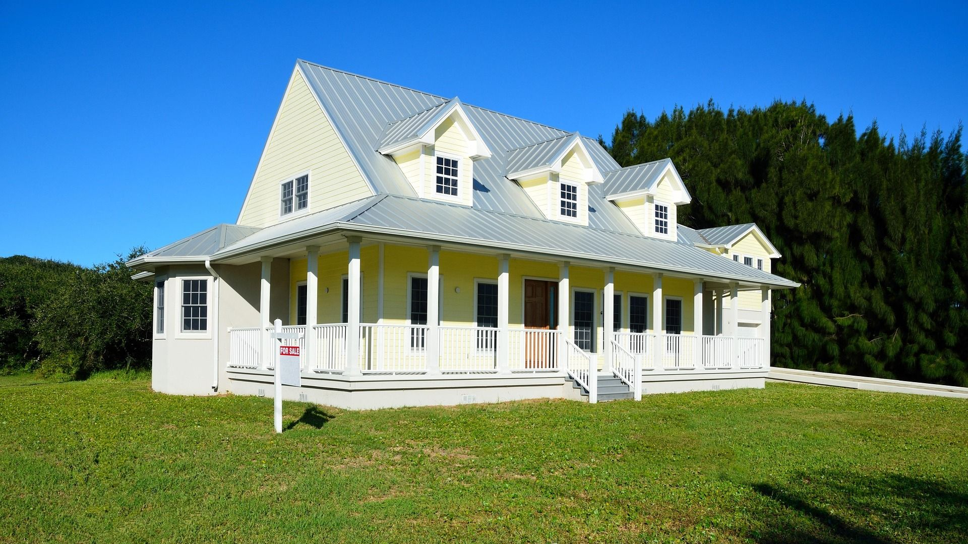 Yellow house with white trim, porch, and metal roof on green lawn.