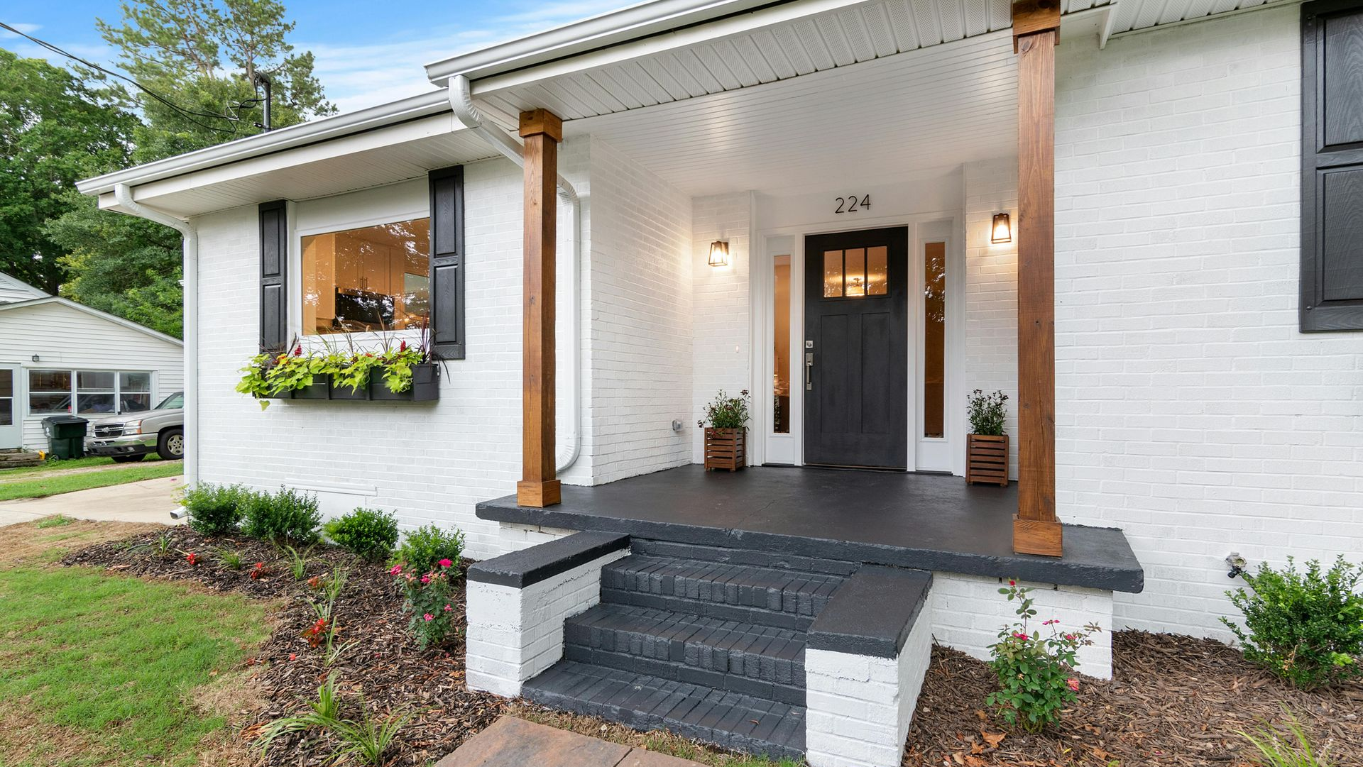 White brick house with dark gray porch, steps, and door. Brown columns, black shutters, and flower boxes.