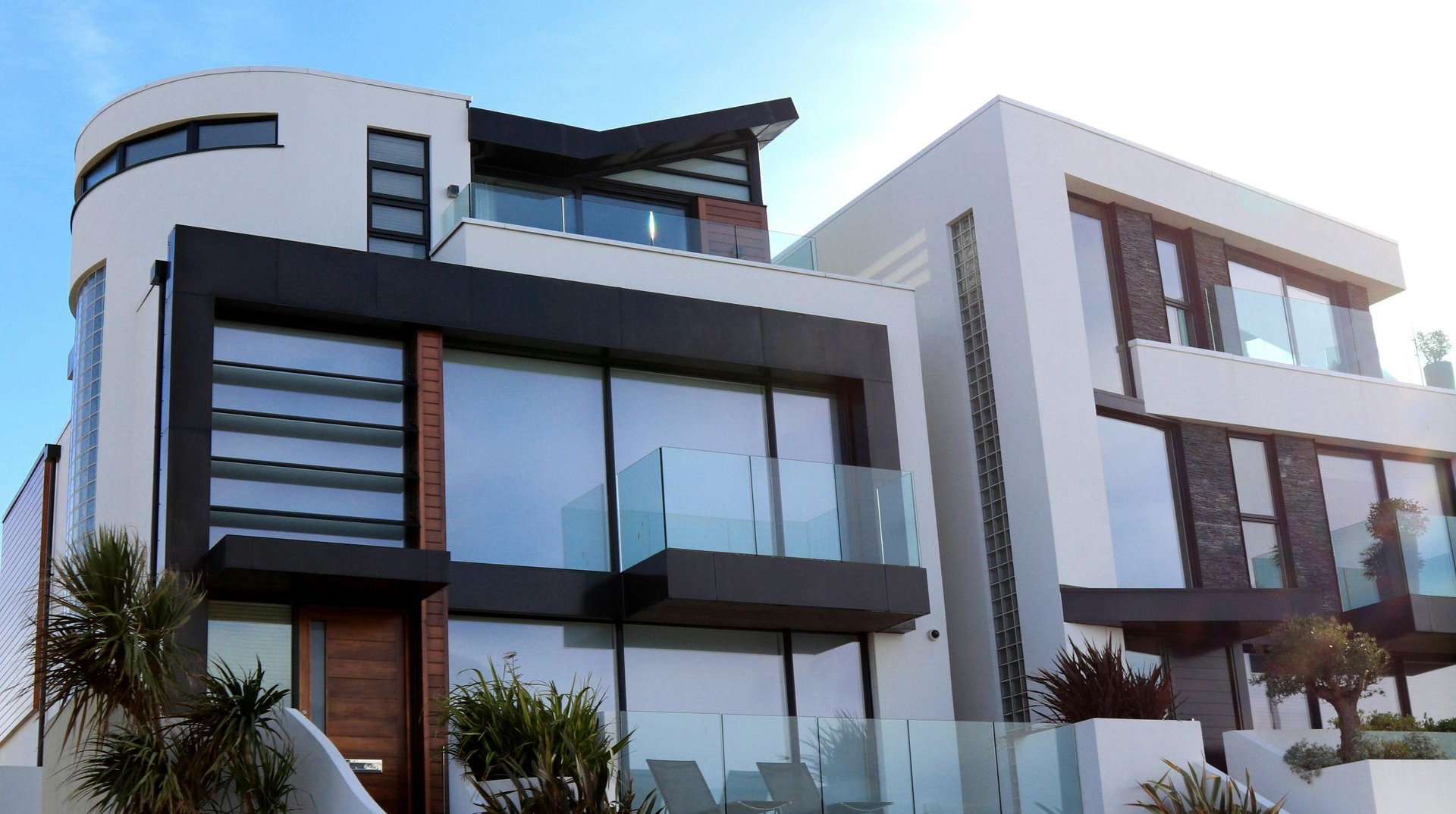 Modern white house with dark trim and large windows, blue sky in background.