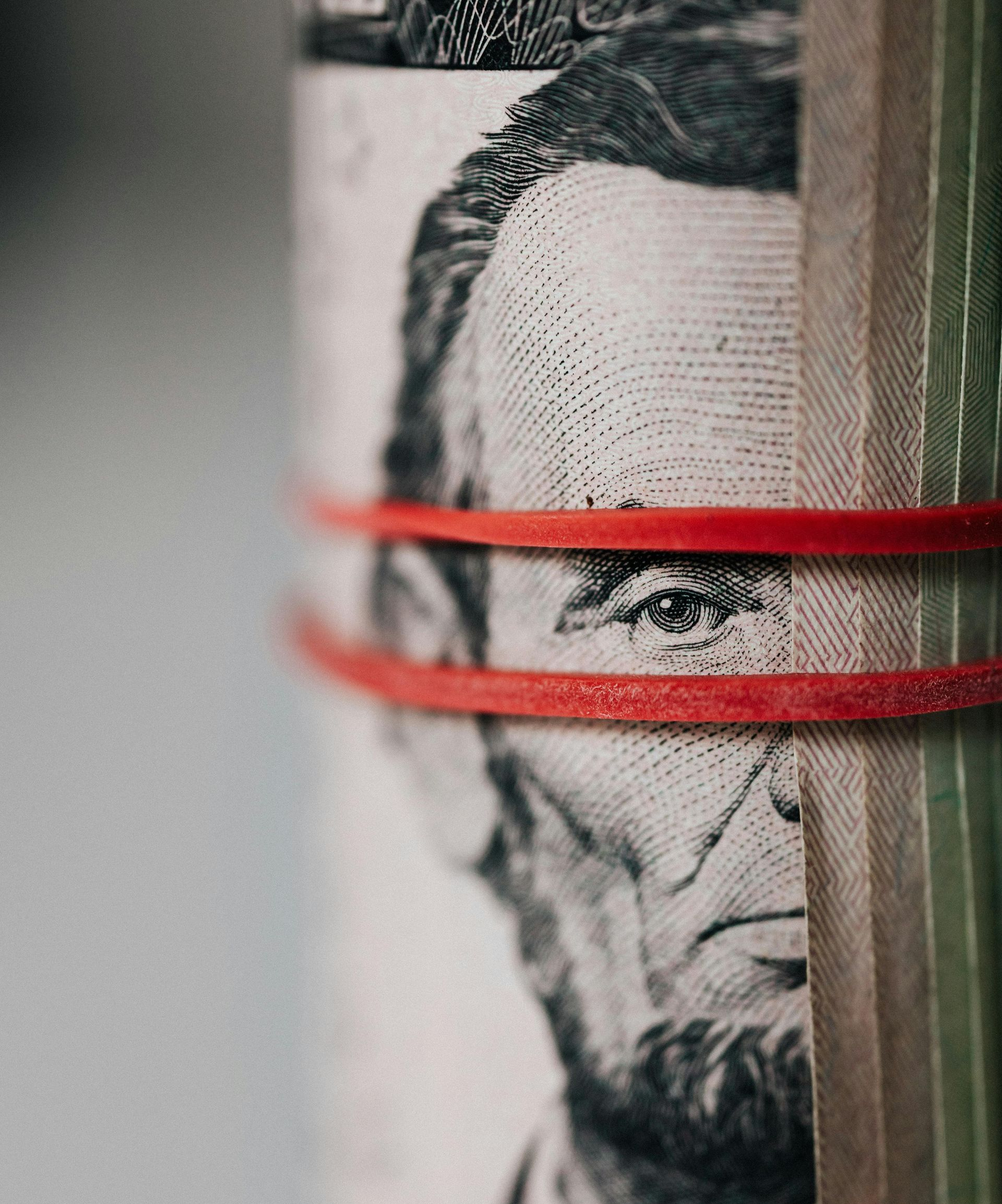 Roll of US five-dollar bills secured with red rubber bands.