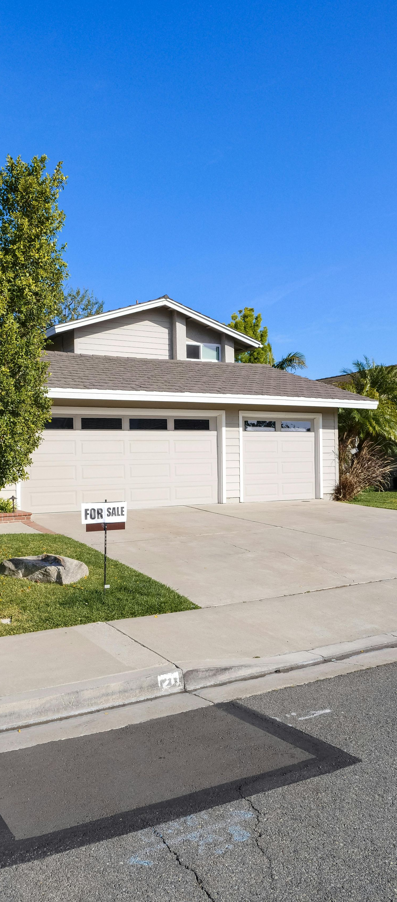 Two-story house with a light-colored garage, driveway, and tree in front against a blue sky.
