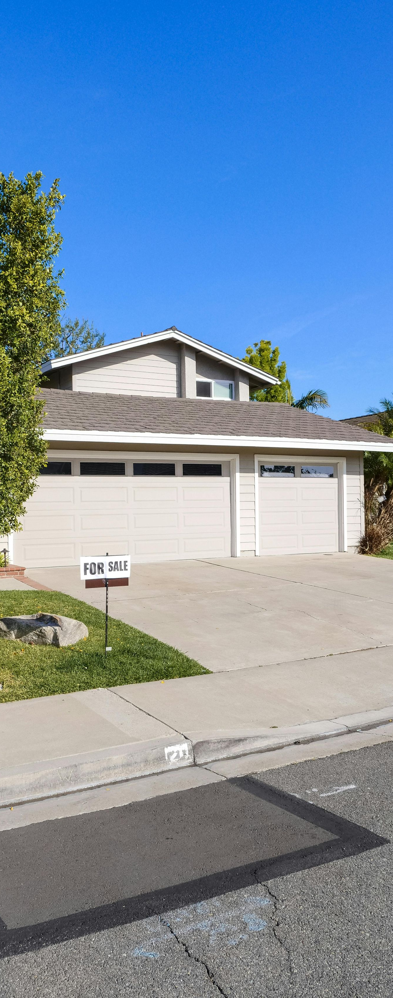 Two-story house with a light-colored garage, driveway, and tree in front against a blue sky.