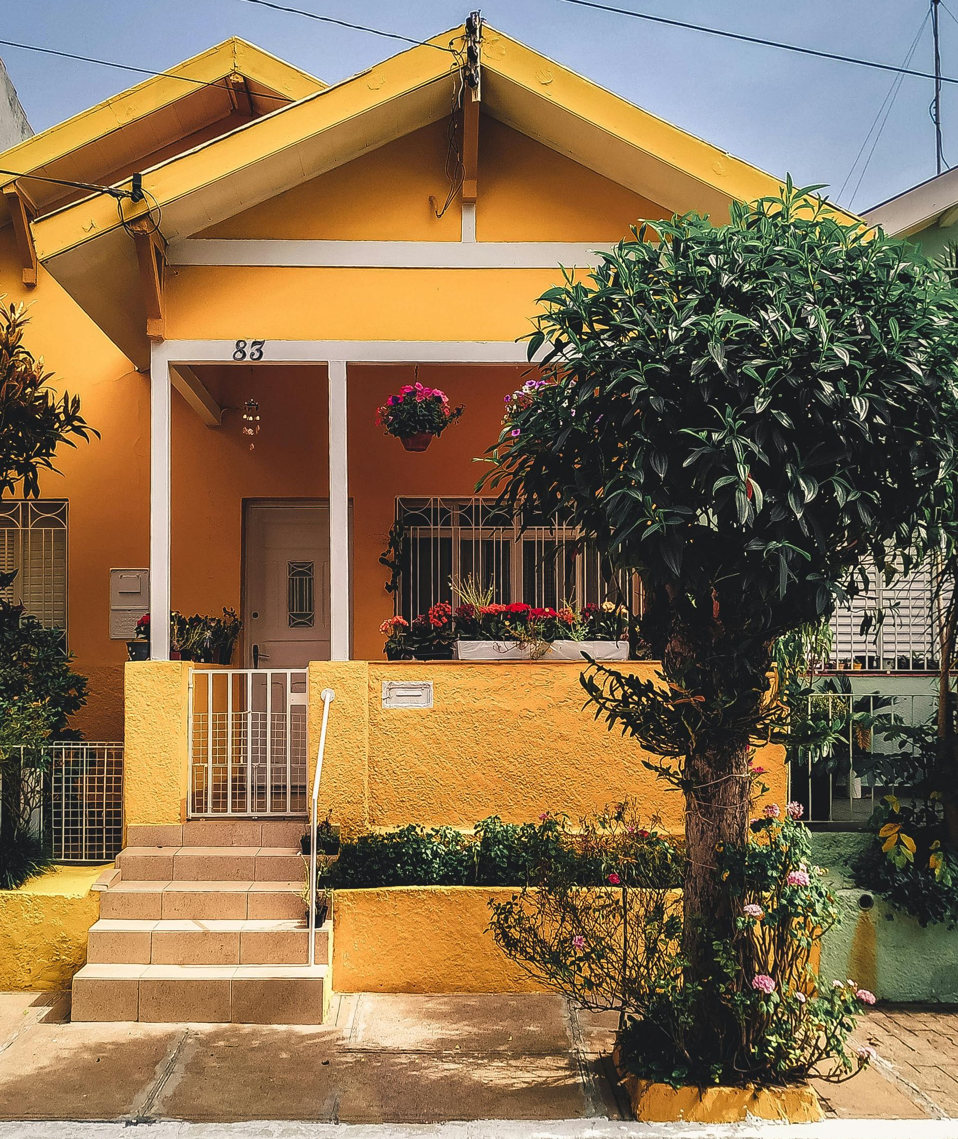 Yellow house with porch and small steps leading to the front door. Flowers in window boxes and hanging baskets.
