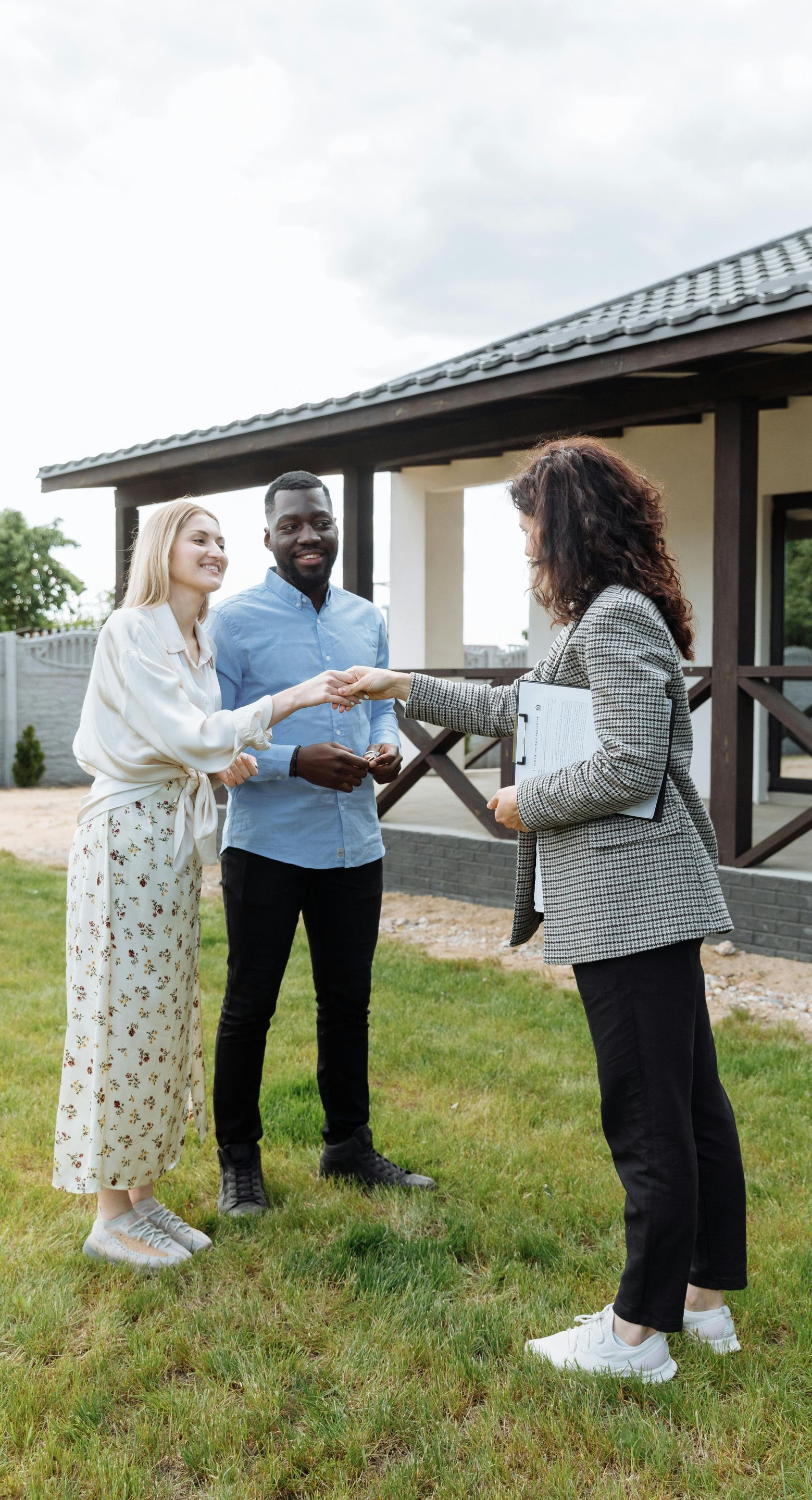Real estate agent shaking hands with a couple in front of a house.