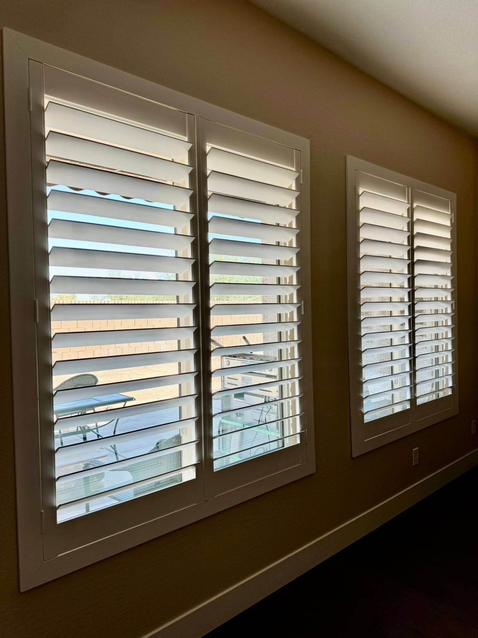 Two white shuttered windows on a tan wall, partially open.