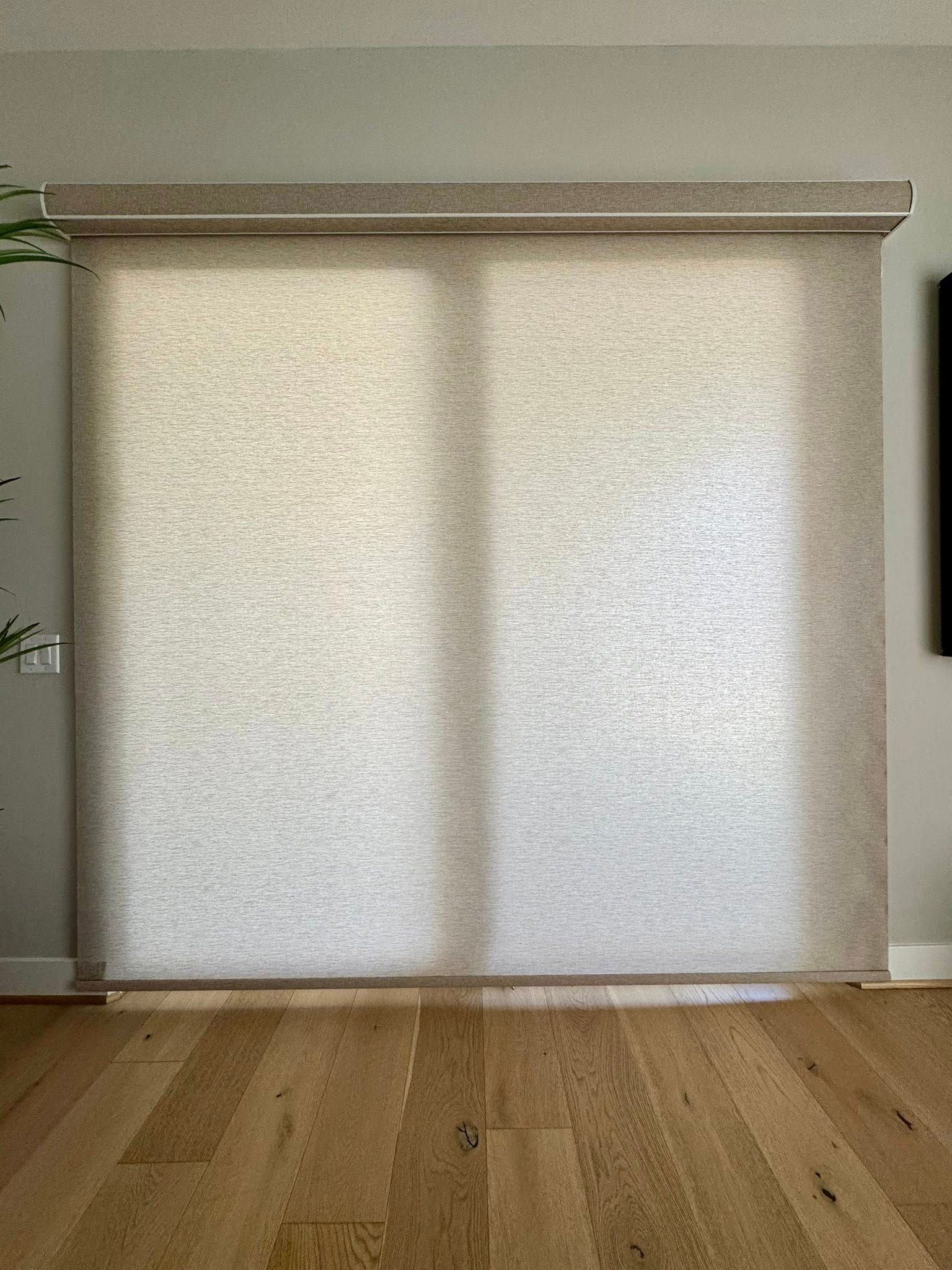 Roller shade on a window, casting shadows on wood flooring. Light beige fabric, neutral colors.