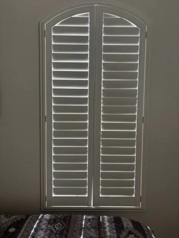 White arched window shutters in a neutral-colored room, partially covering the view.