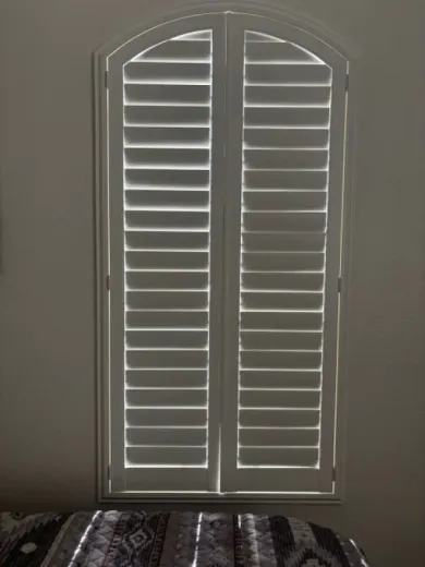 White arched window shutters in a neutral-colored room, partially covering the view.