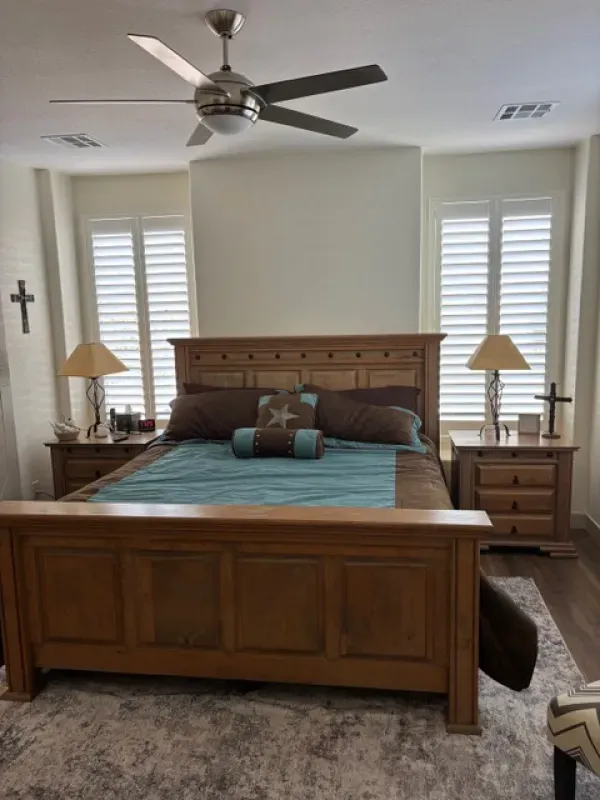 Bedroom with wooden bed, teal bedding, shutters, lamps, and a ceiling fan.