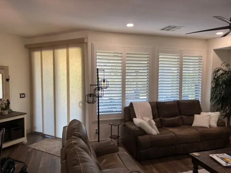 Living room with brown sofa, white shutters, and sliding panel shades.