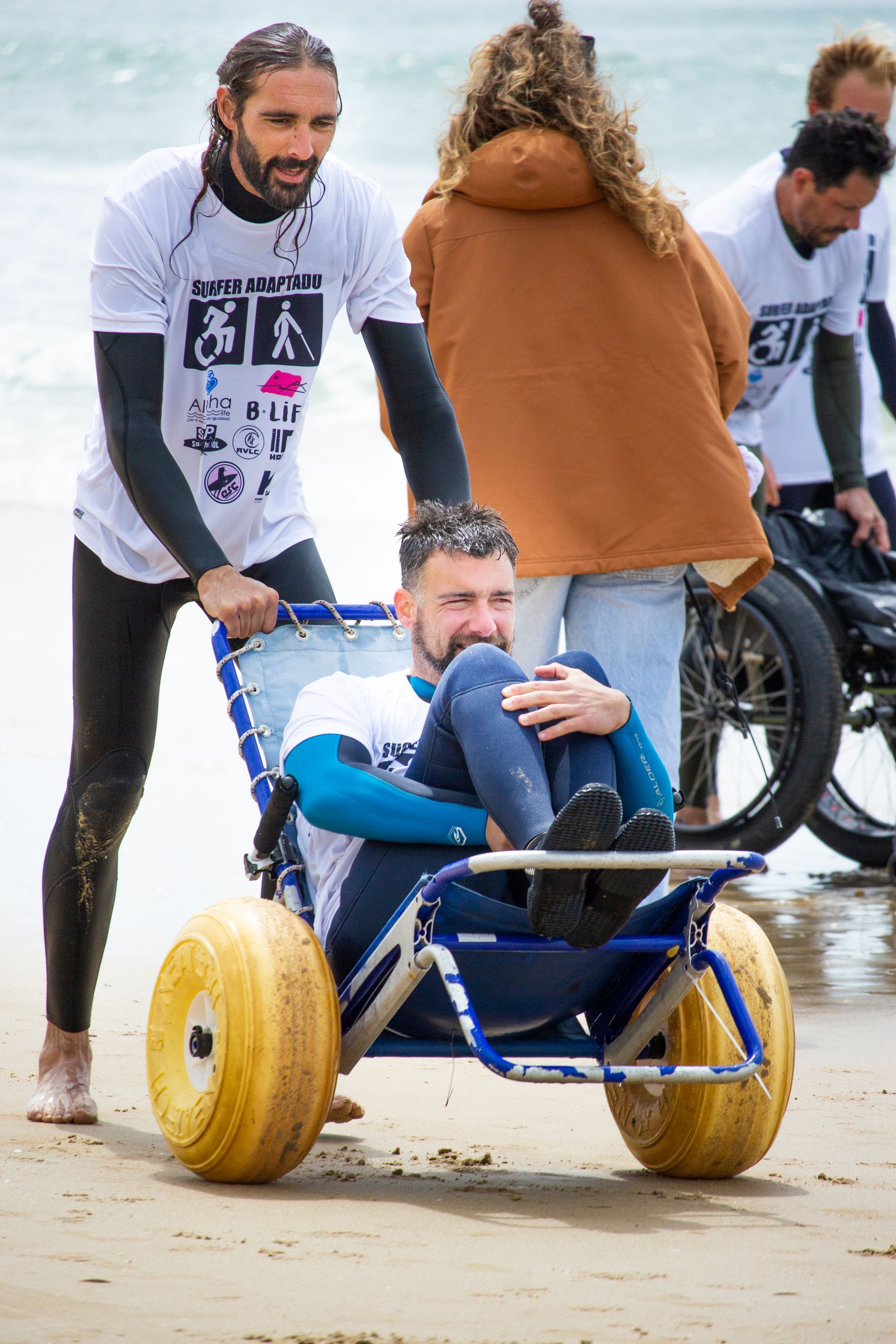 Un instructor lleva en la silla de ruedas anfibia a un alumno  tras disfrutar de las olas.