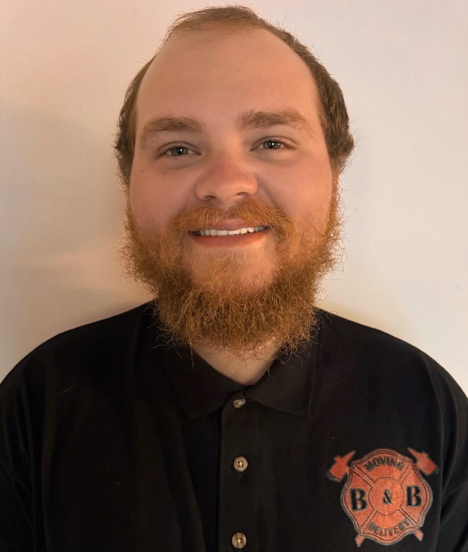 A man with a beard is wearing a black shirt with the letter b on it