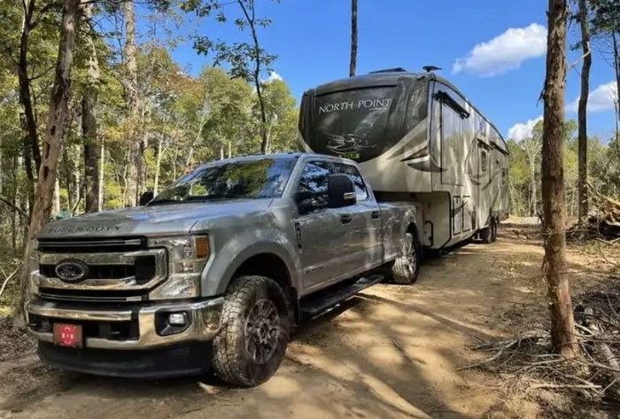 A truck is towing a rv down a dirt road.