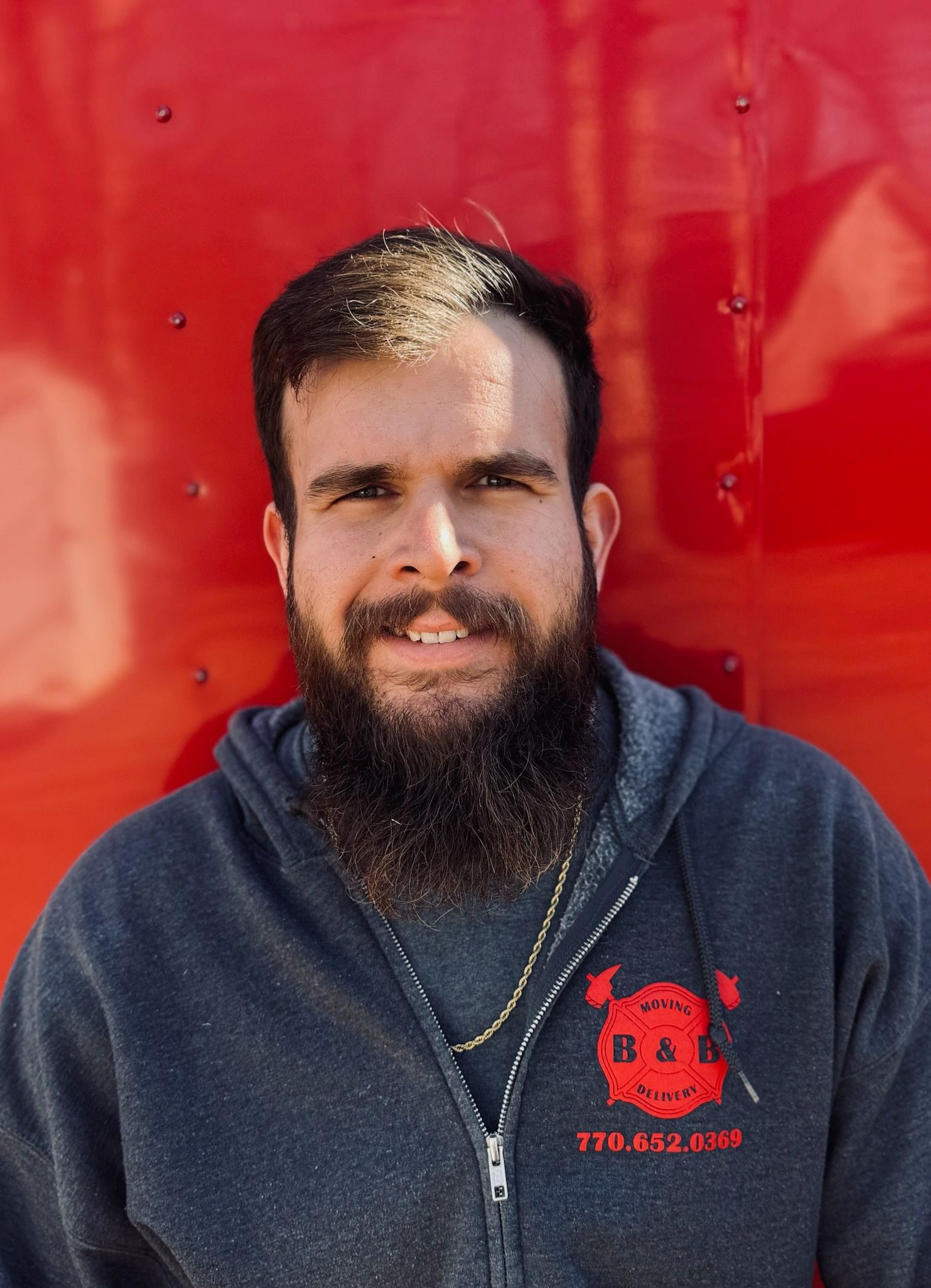 A man with a beard is wearing a red shirt with the letter b on it