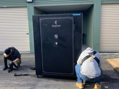 Two men are moving a large safe in front of a building.