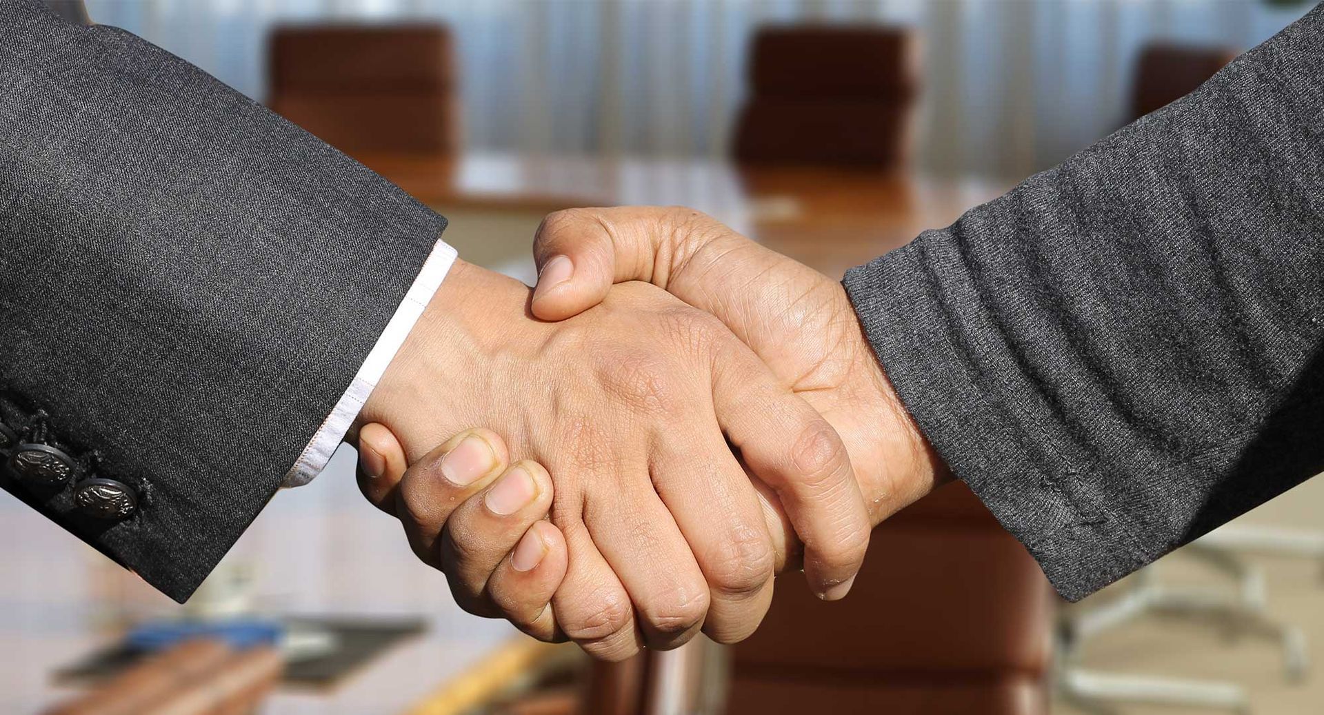 Two people in business suits shaking hands in an office setting.