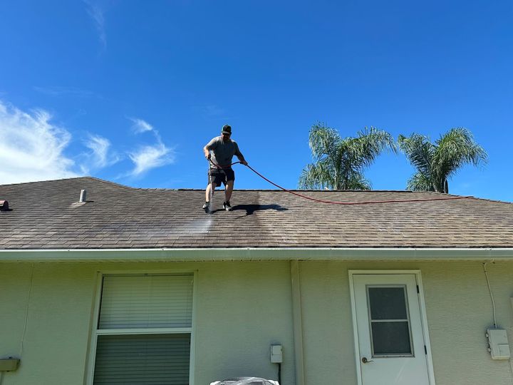 A man is cleaning the roof with soft wash techniques.