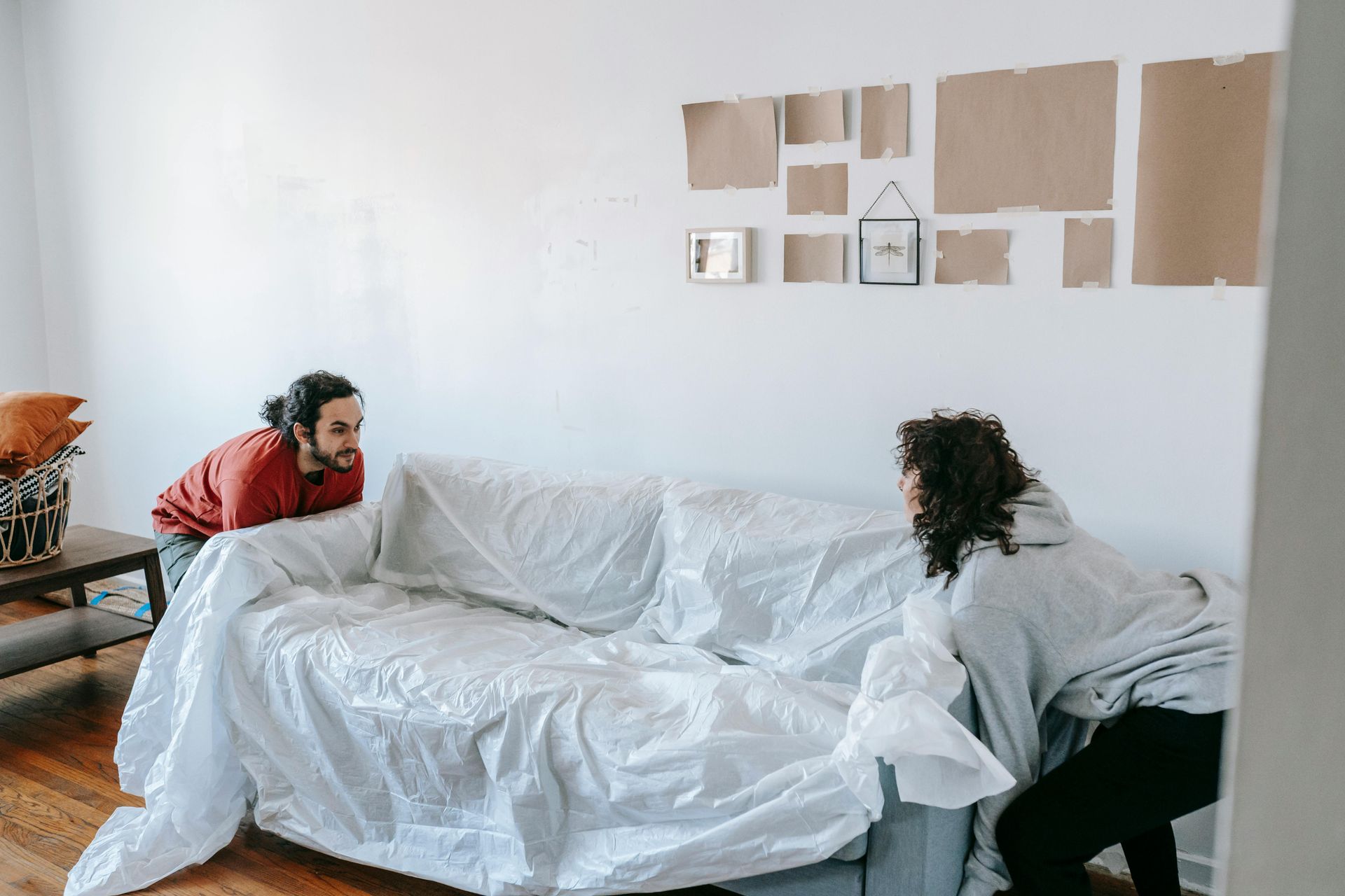Two people working together to move a mattress covered in protective plastic wrap