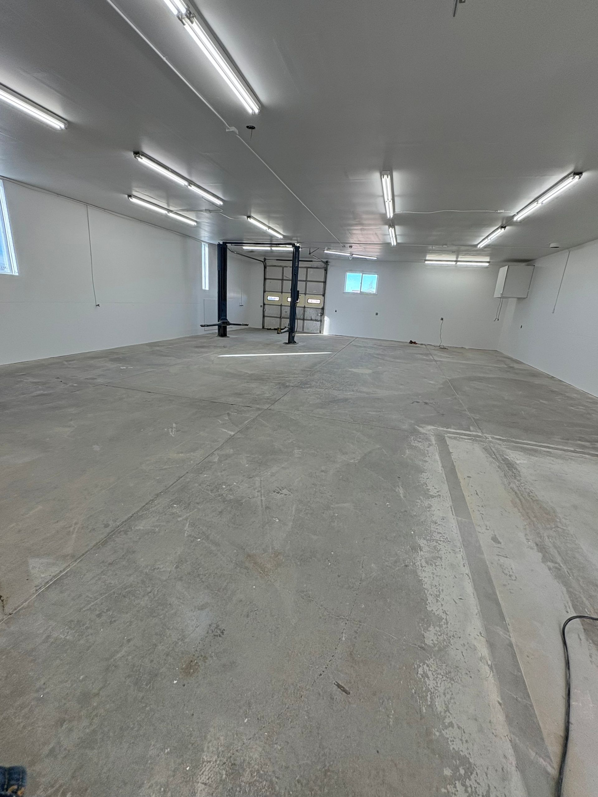 An empty, white-walled commercial space with a grey concrete floor and overhead strip lighting.