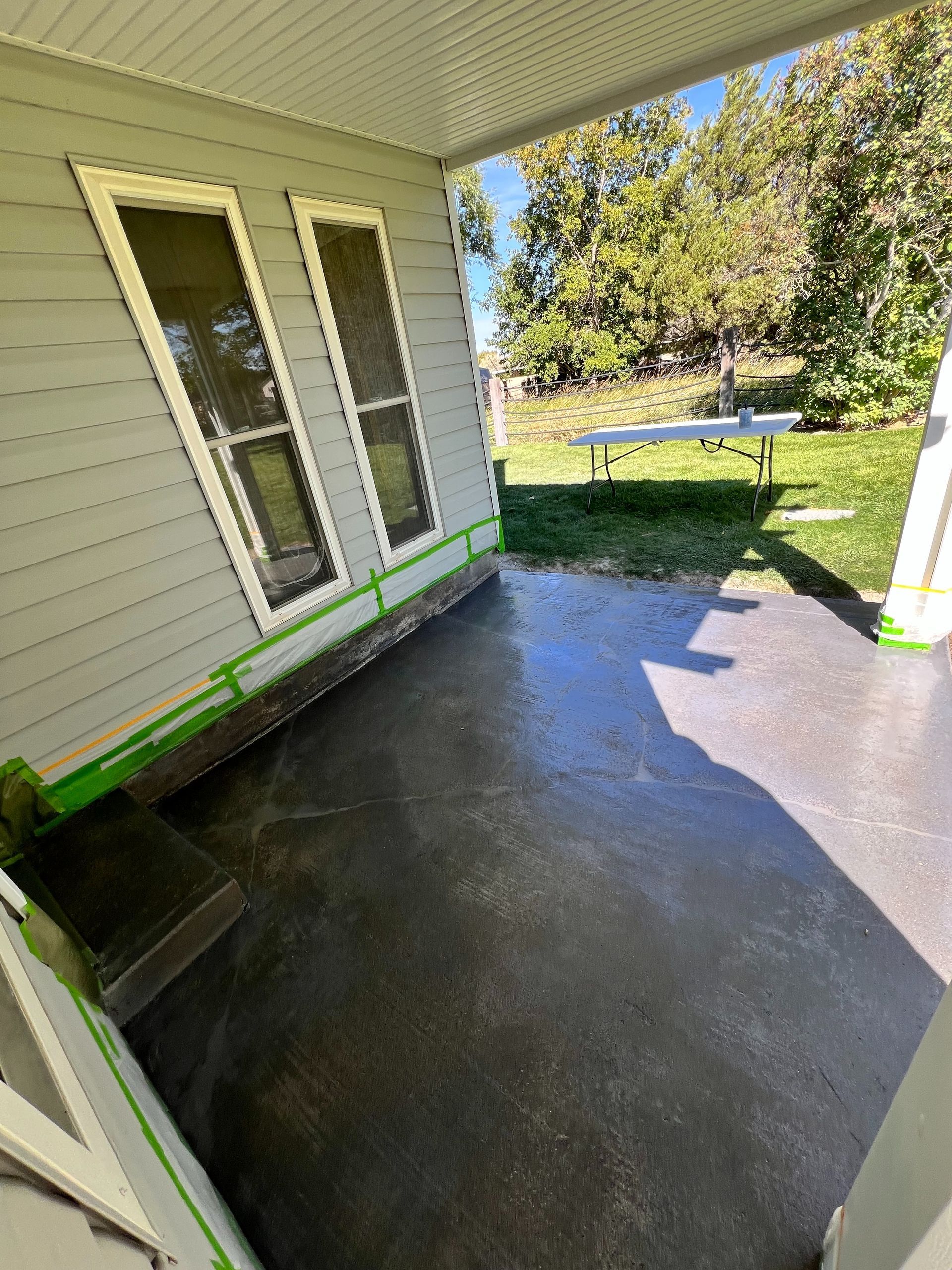 A grey-walled porch with windows and green painter’s tape applied along the bottom edge, overlooking a sunny lawn.