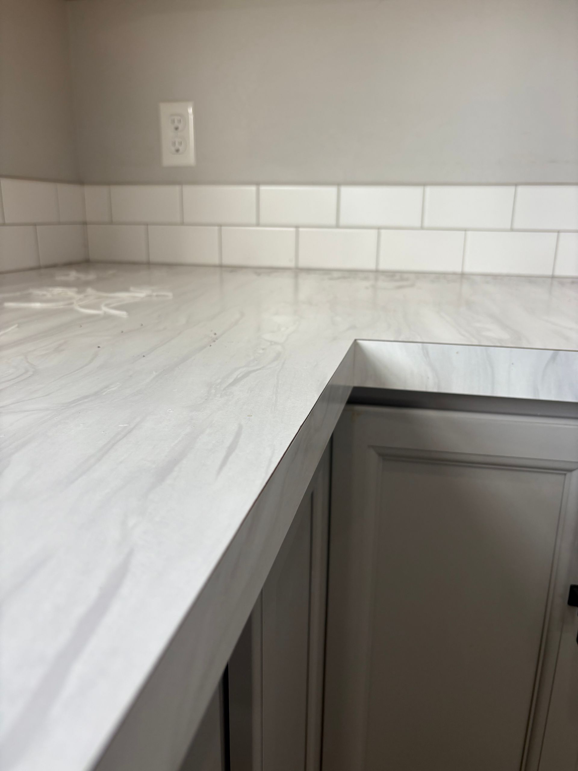 White faux-marble countertop with a white subway tile backsplash and gray cabinets in a kitchen setting.