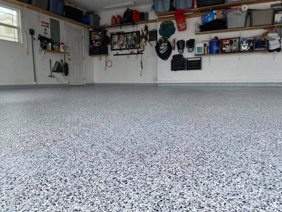 A bright, clean garage featuring a newly applied grey and white speckled epoxy floor with wall-mounted storage and shelves.