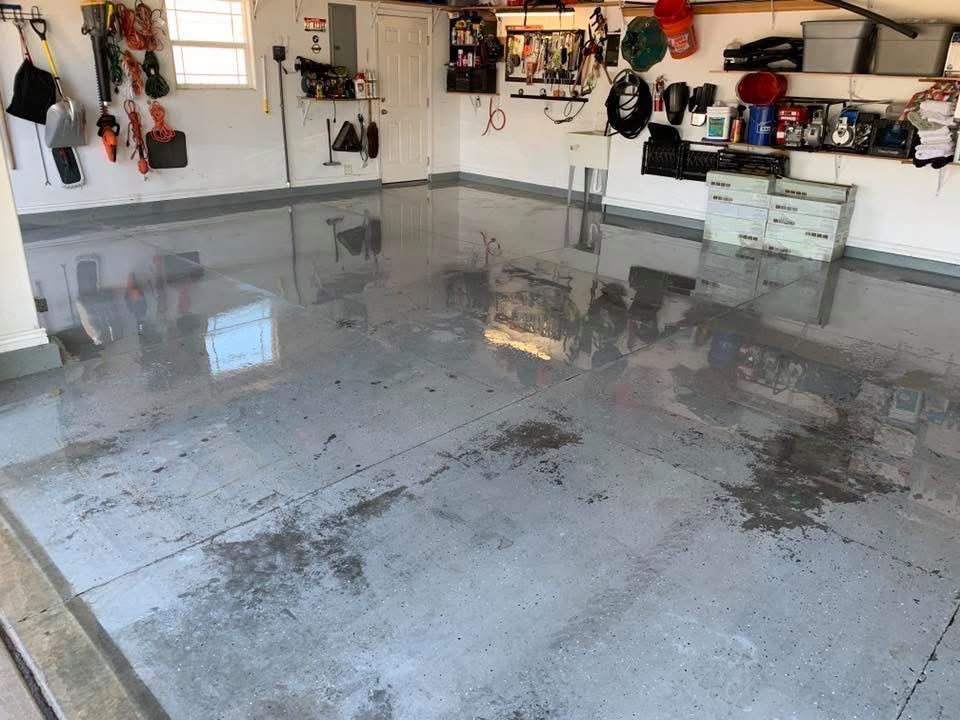 A garage with a high-gloss gray epoxy floor, cluttered shelves, and tools hanging on white walls.