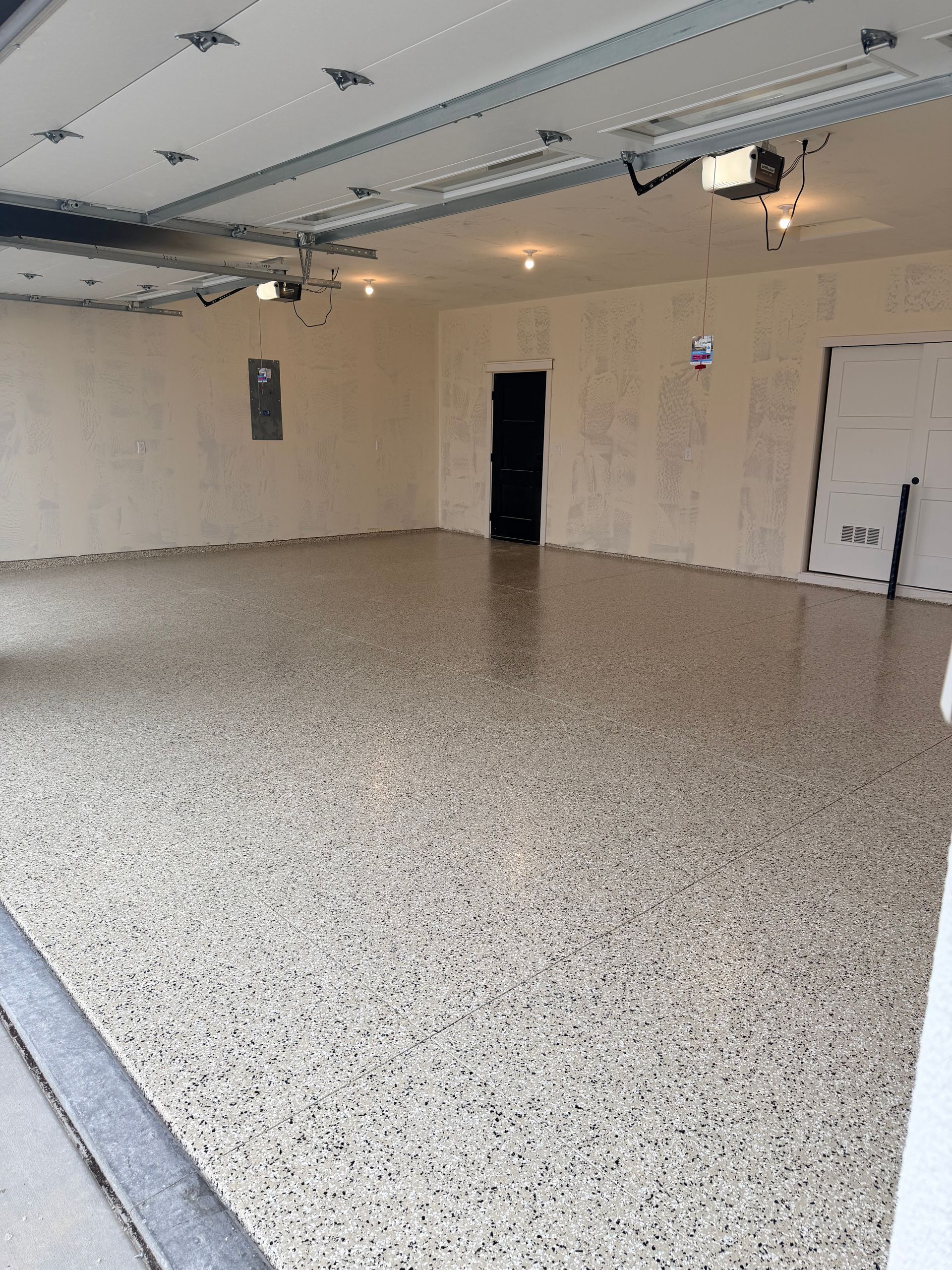 A clean, empty garage with a polished, beige and grey speckled epoxy floor and cream-colored walls.