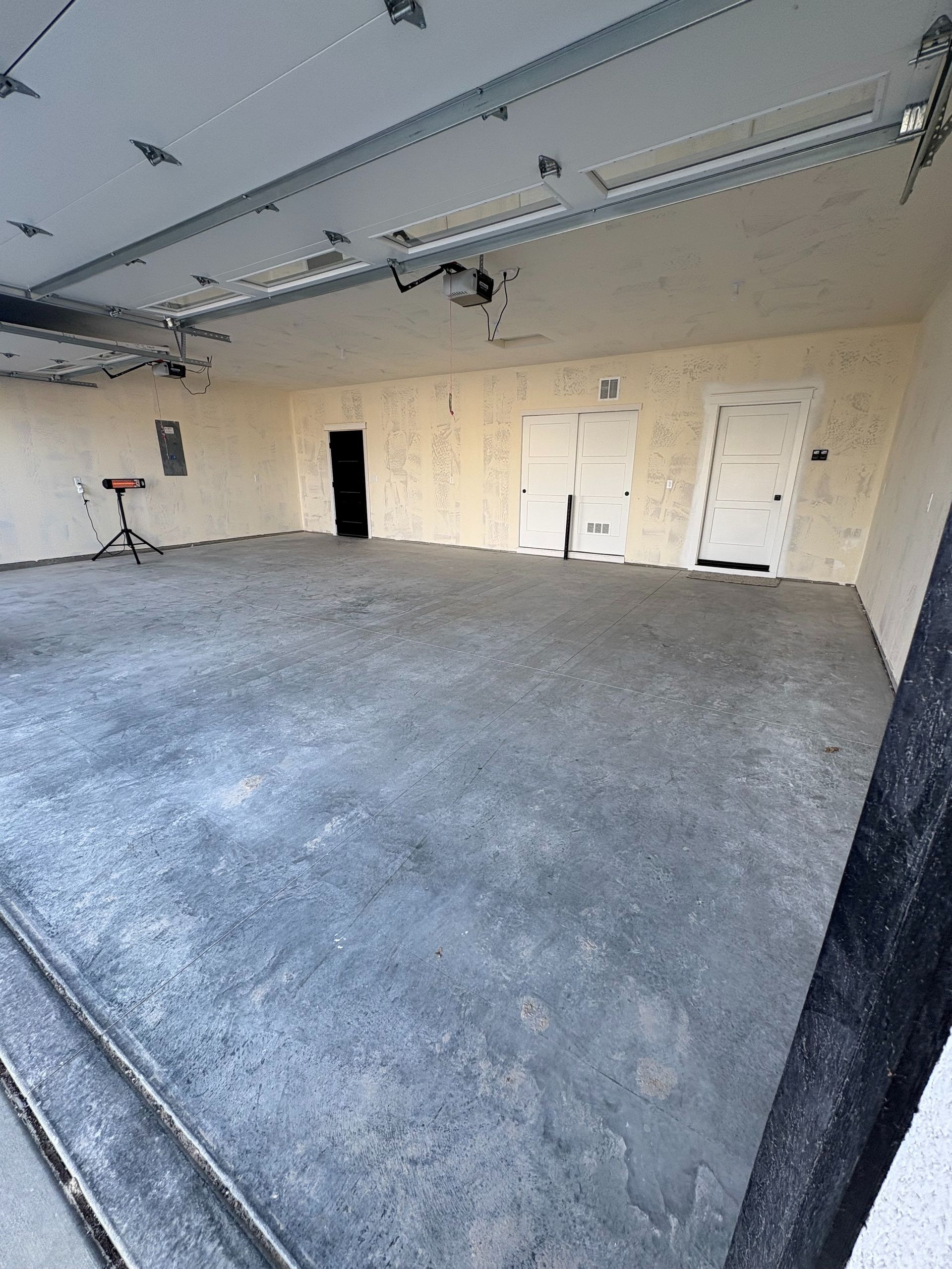 An empty, spacious residential garage with a concrete floor, white walls, two closed doors, and a small tripod stand.