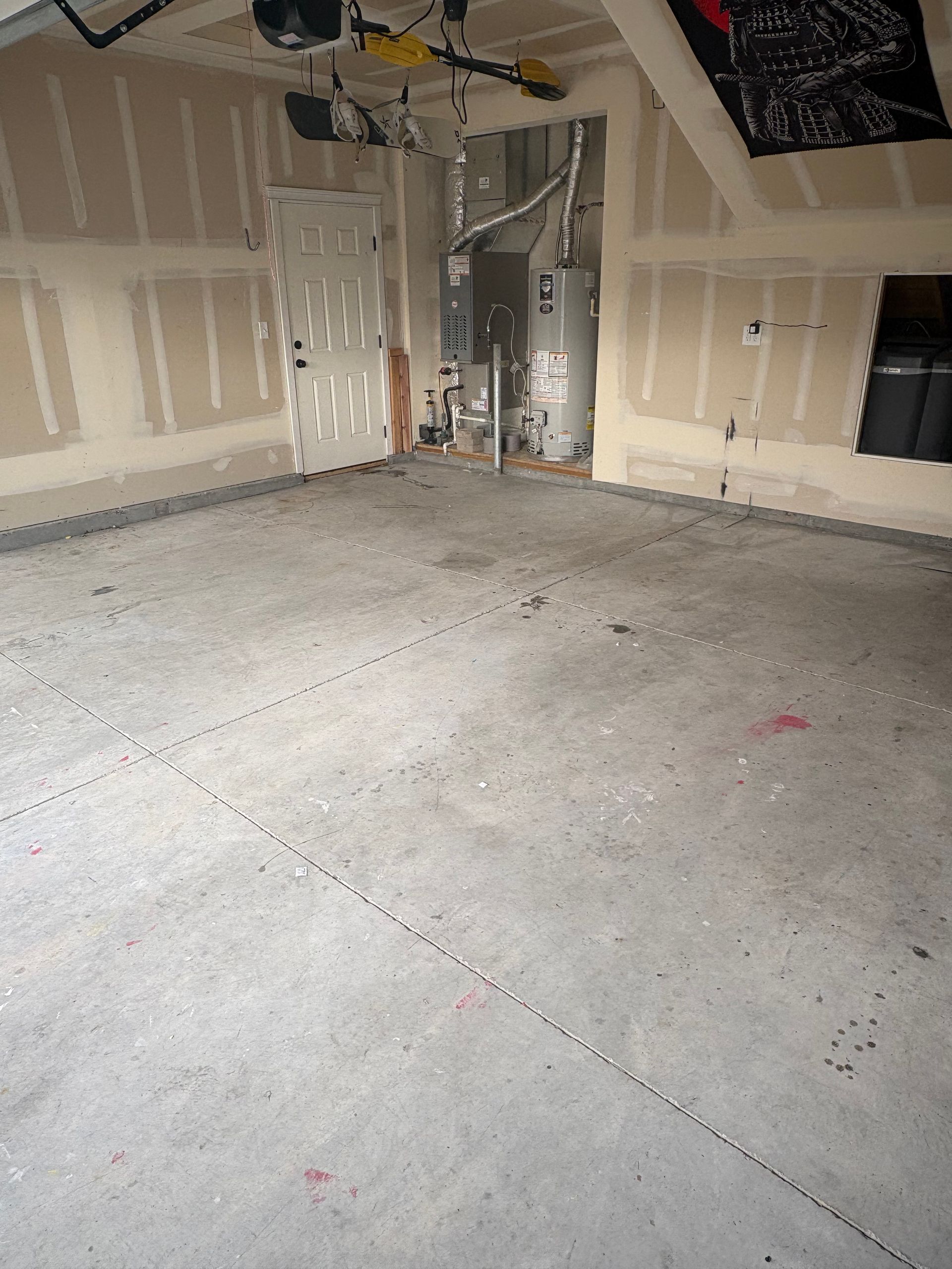 An unfinished garage with gray concrete flooring, drywall-covered walls, a white interior door, and a utility closet.