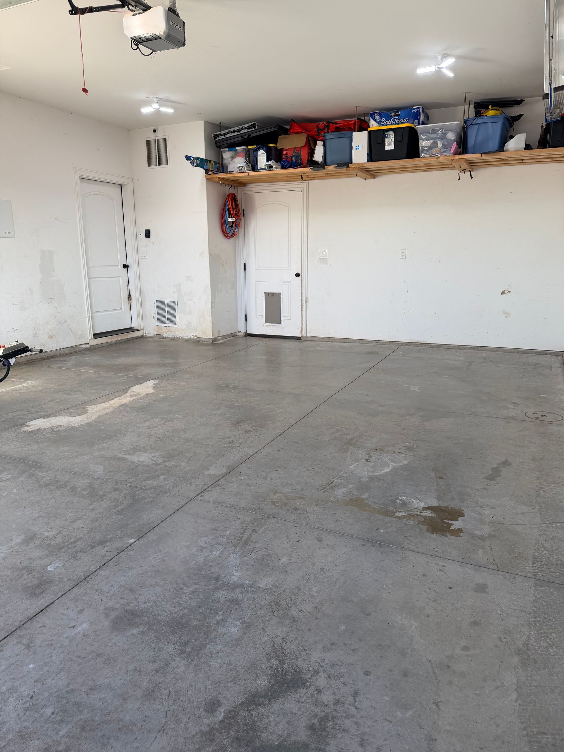 A gray concrete garage floor with a wooden storage shelf mounted on the back wall above a white door.