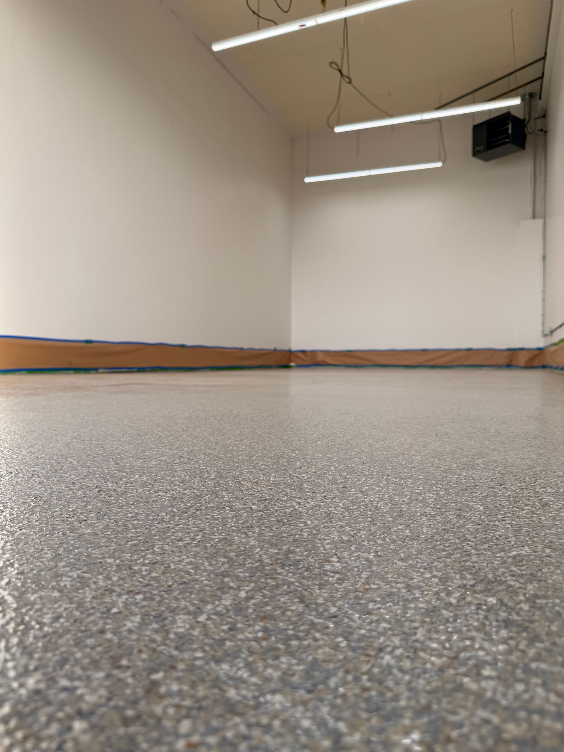 Empty garage interior with grey speckled epoxy flooring and three linear LED lights hanging from the ceiling.