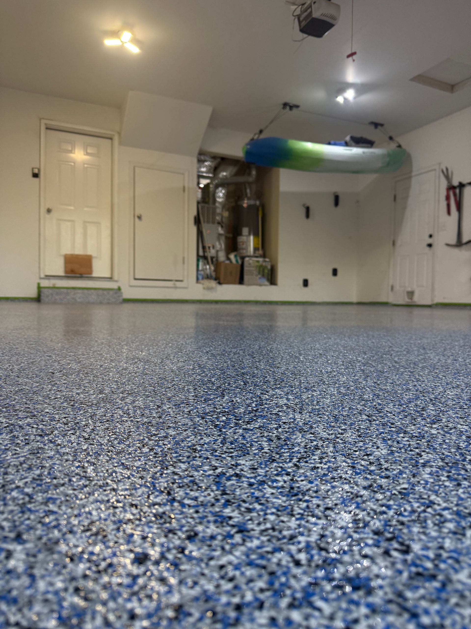 A low-angle view of a garage with a glossy blue and white flecked epoxy floor and a kayak suspended from the ceiling.